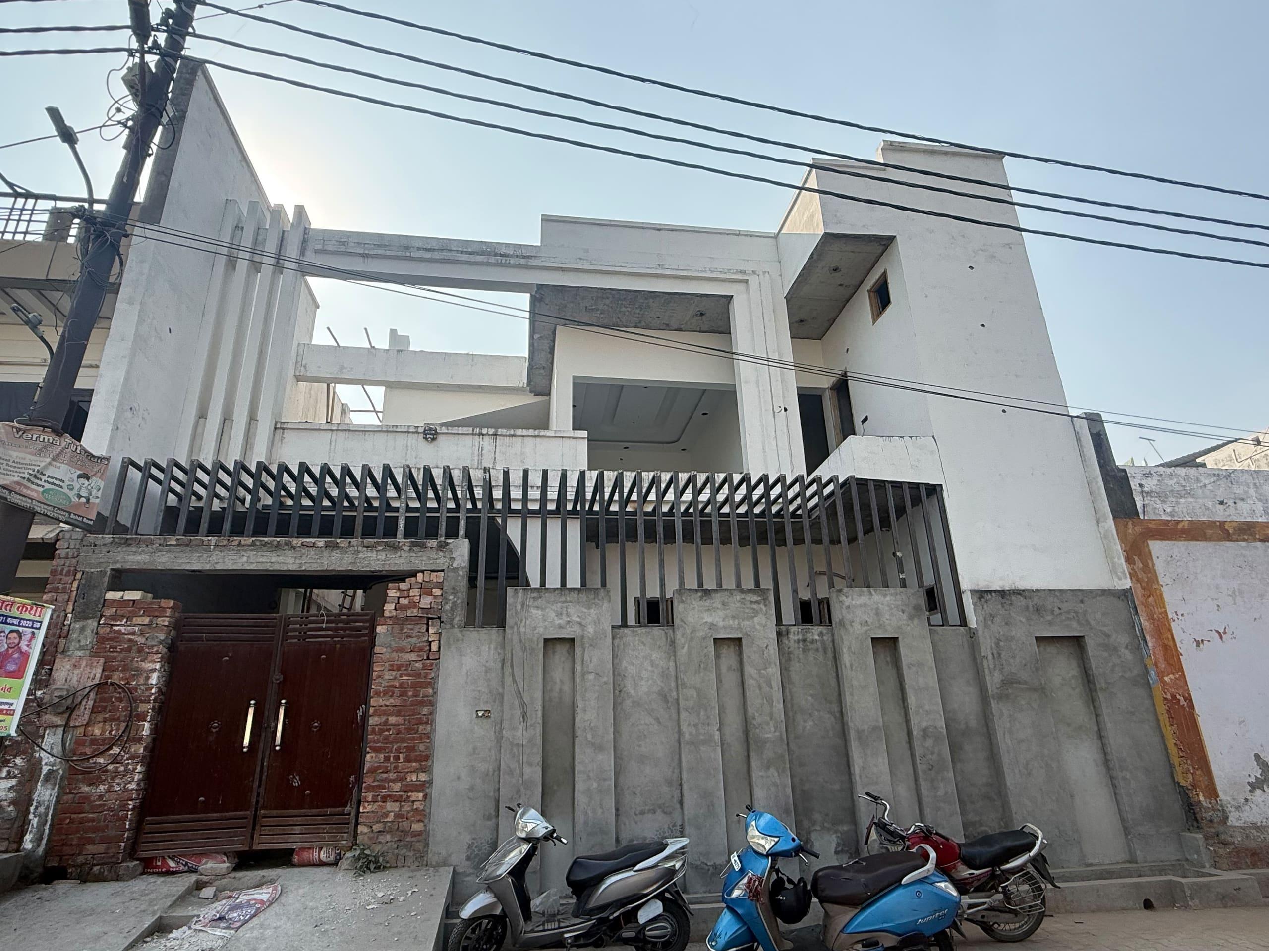 The same house mid-construction, exposed concrete with a jali screen fence at street level